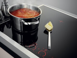 Een lepel met boter rust veilig op de koele kookplaat naast een borrelende pan met tomatensaus