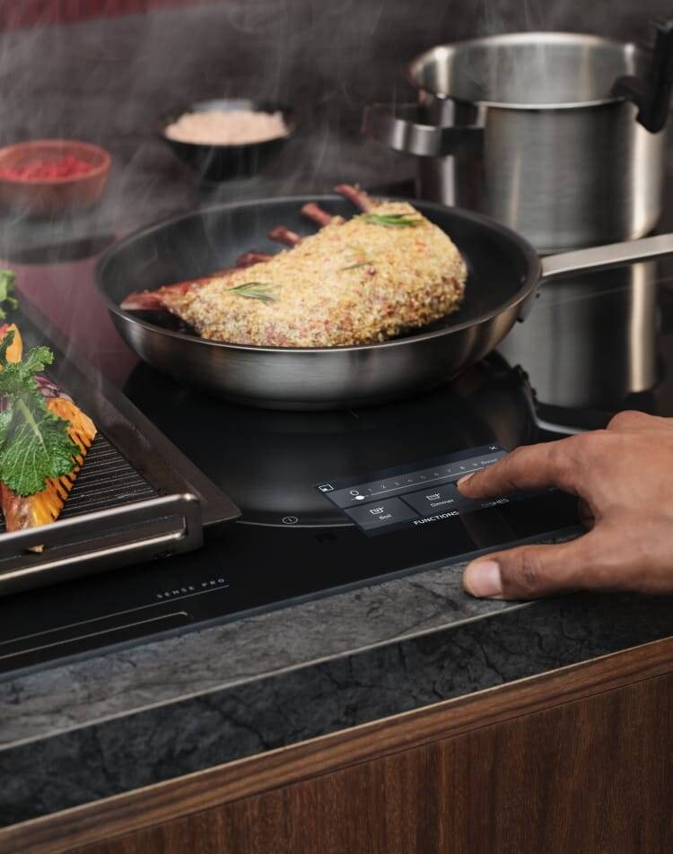 Un doigt touche le panneau de commande d’une taque de cuisson à induction pendant la préparation des aliments.