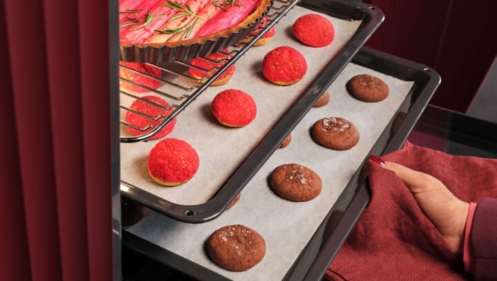 Een persoon haalt een bakplaat met gebakjes uit de oven.