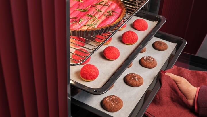 Een persoon haalt een bakplaat met gebakjes uit de oven.