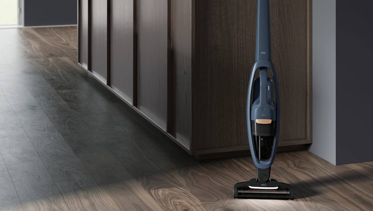 Draadloze steelstofzuiger van AEG in een gang.