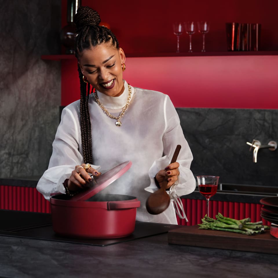 Femme cuisinant dans une cuisine rouge bordeaux où des casseroles sont posées sur une plaque à induction AEG.
