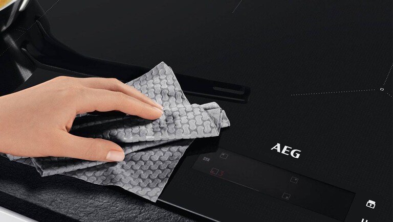 Une plaque à induction AEG nettoyée par quelqu'un avec un chiffon.
