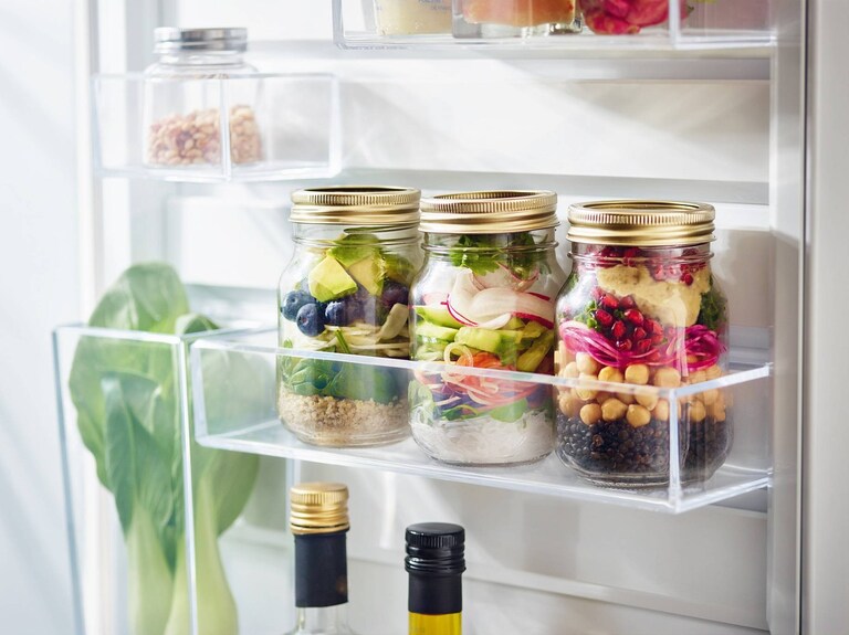 Un gros plan d’une porte de réfrigérateur ouverte, avec des aliments rangés à l’intérieur.