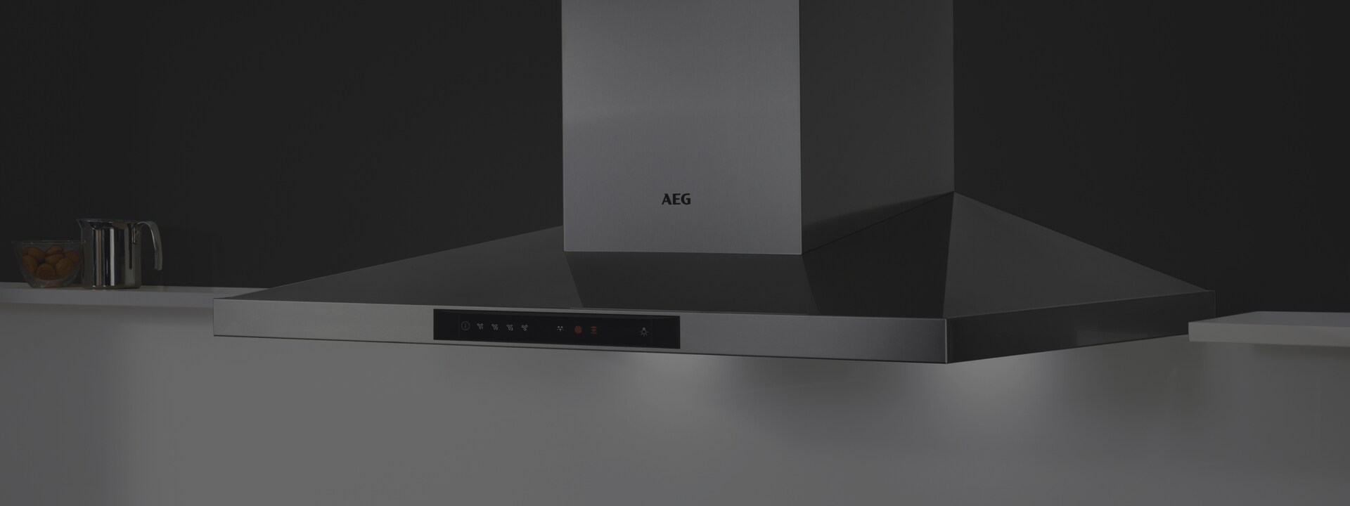 Une cuisine avec un mur noir sur lequel est accrochée une hotte murale AEG qui fonctionne.