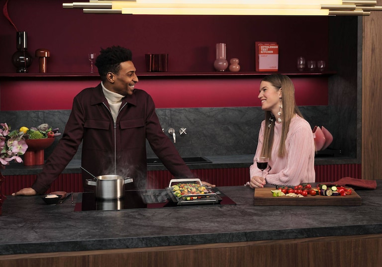 Man en vrouw in keuken aan het praten en eten aan het bereiden op een AEG inductiekookplaat