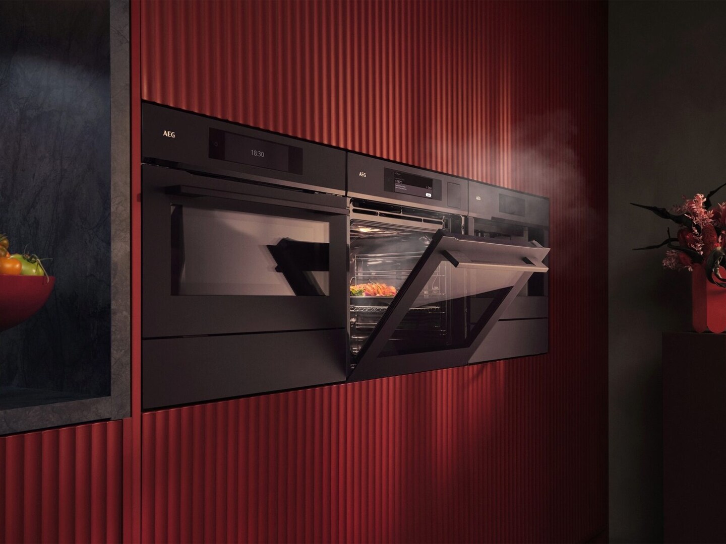 Een bordeaux rode keukenwand met verschillende AEG inbouwovens waarbij er 1 open staat 