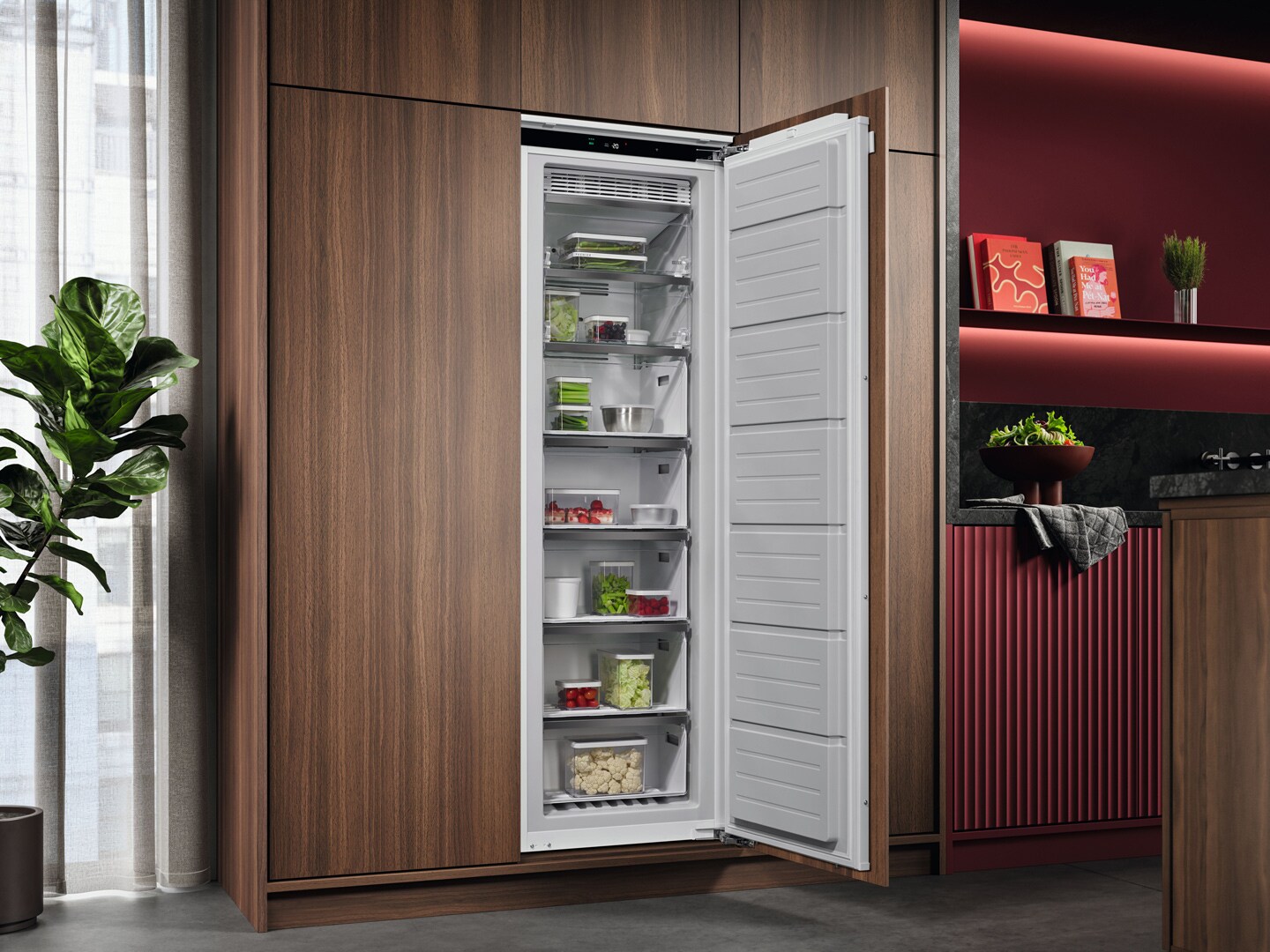 Une cuisine avec des placards rouge bordeaux et un congélateur AEG encastré à 7 tiroirs, ouvert et rempli de nourriture.